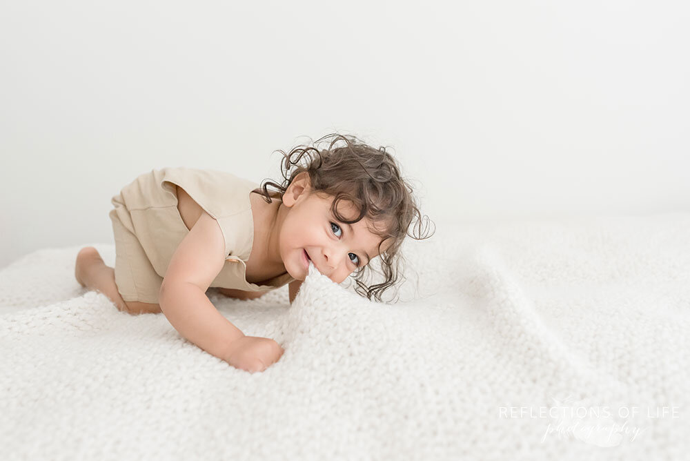 Little boy bites the white blanket with his teeth in Niagara Region natural light studio Grimsby