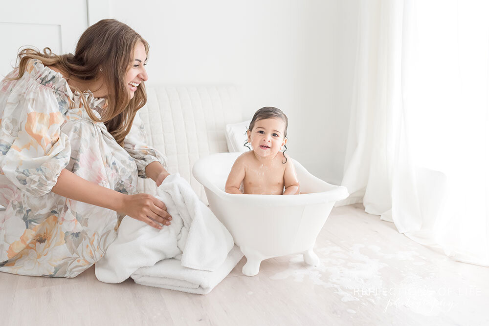 Mom is going to pick up her baby boy with a white towel and dry him off after his bath in the tiny tub Niagara Region baby and family photoshoot
