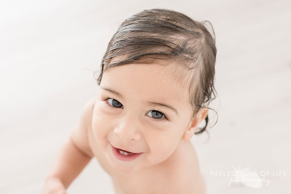 Baby boy smiling at the camera with wet hair after bathtub photoshoot in Grimsby Ontario Canada