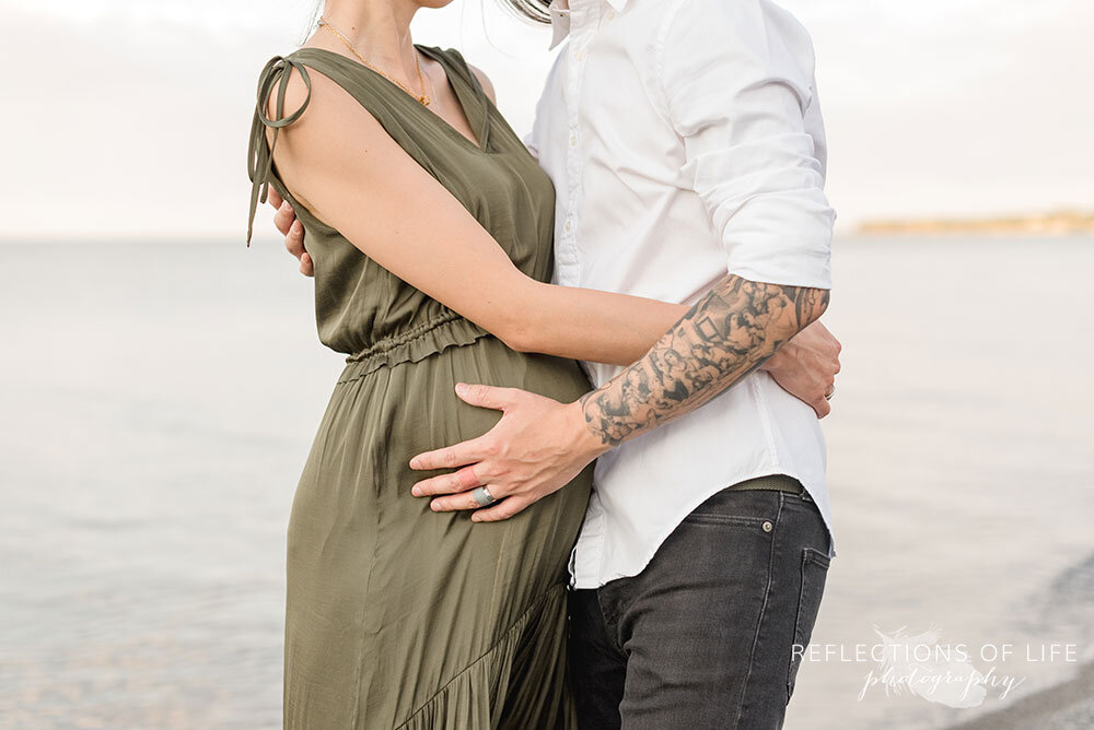 Soon to be daddy and pregnant mom embrace on the beach in Niagara Ontario Canada photoshoot