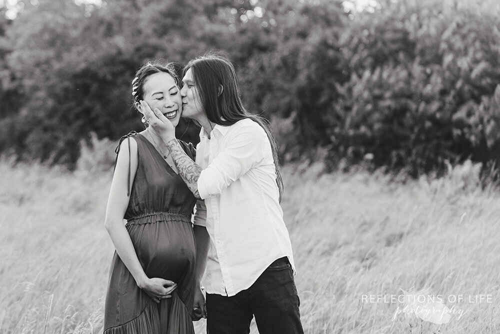 Daddy kissing his wife's cheek during pregnancy photoshoot in the open field in Grimsby Ontario Canada