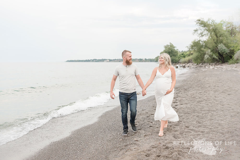 Adorable pregnant couple walking down the beach together in Niagara Ontario Canada