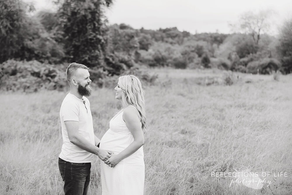 Pregnant couple posing in a field for maternity photography in Grimsby Ontairo Canada