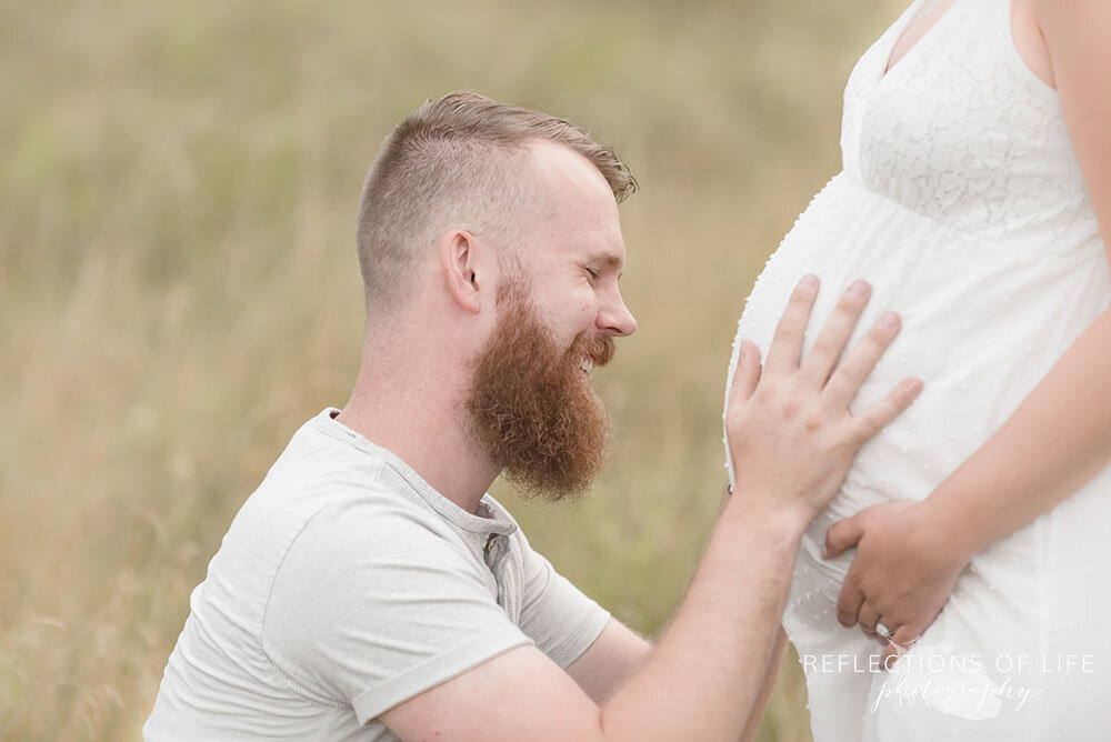 New dad smiles while talking to his unborn baby and placing his hands on his wife's belly Grimsby Maternity Photos