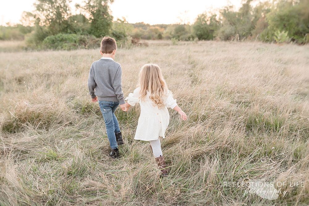 Siblings walking into a field together Niagara Region family photography