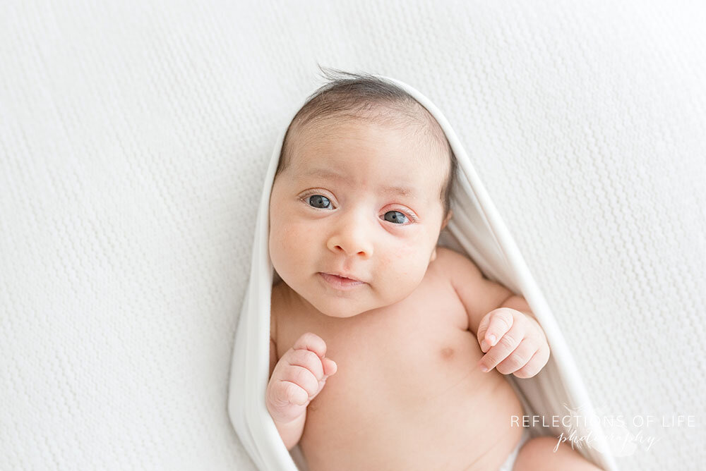 Adorable awake baby wrapped in white muslin swaddle blanket