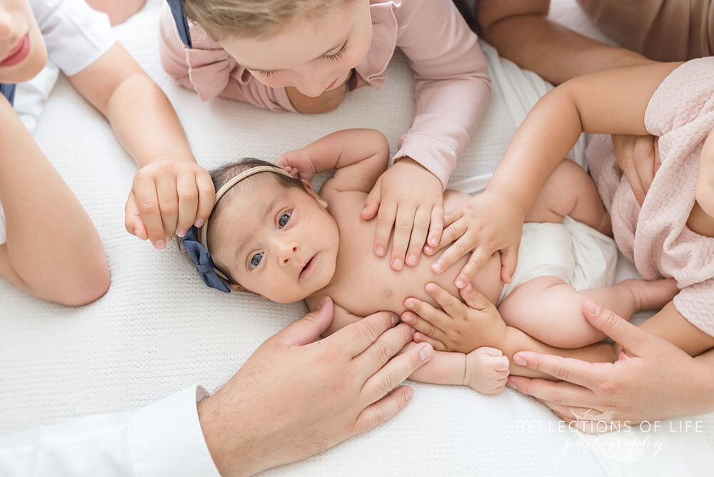 Newborn baby girl surrounded by her family with their hands on her Niagara Ontario
