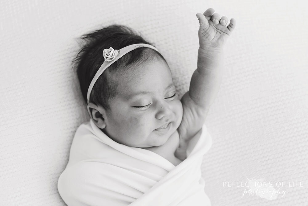 Newborn baby stretching with arm up in the air in black and white