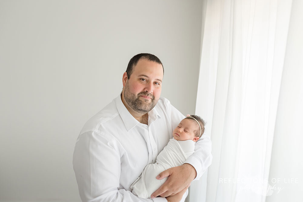 Daddy holds his newborn baby girl in light bright studio in Grimsby Ontario