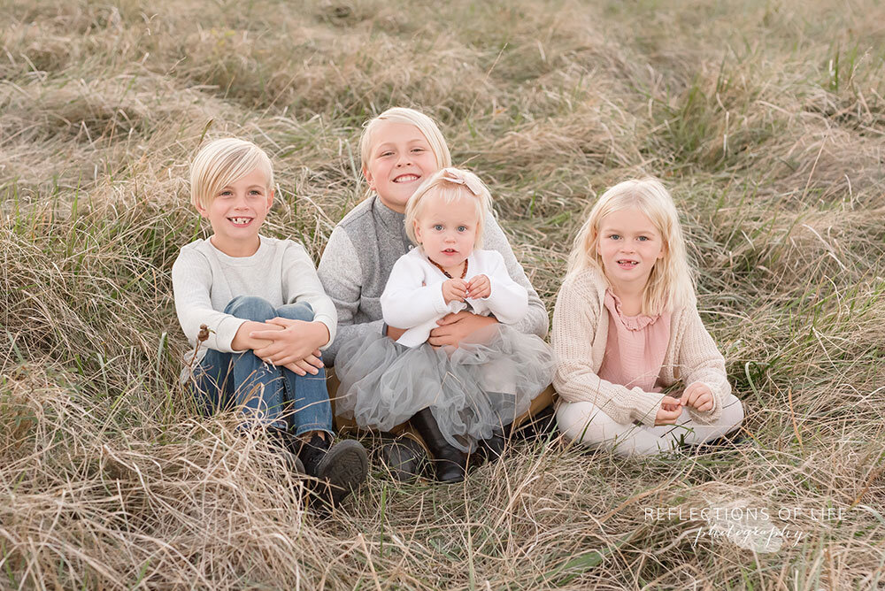 Cute sibling photo of four children sitting on the long grass Grimsby Ontario