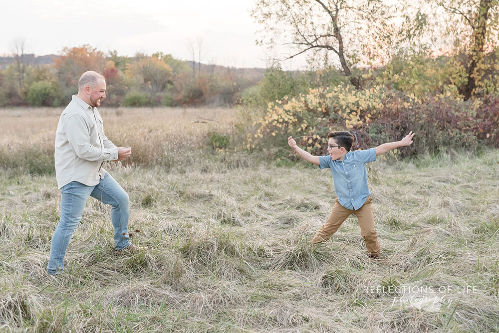 Father and son play swordfight with sticks during family photos in Niagara Region Ontario