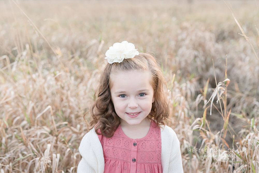 Little girl smiles sweetly at the camera during family photos in the field Grimsby Ontario