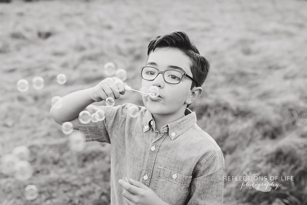 Little boy blowing bubbles during outdoor photoshoot in open field Niagara Ontario Canada