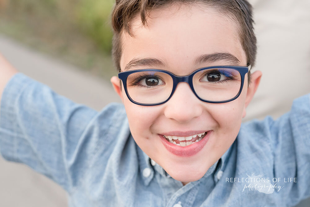 Adorable little boy with glasses smiles at the camera field photoshoot Grimsby Ontario
