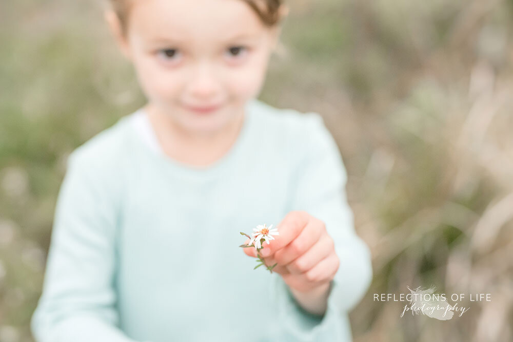 Little girl holds daisy while looking into the camera in green dress Niagara Region Ontario