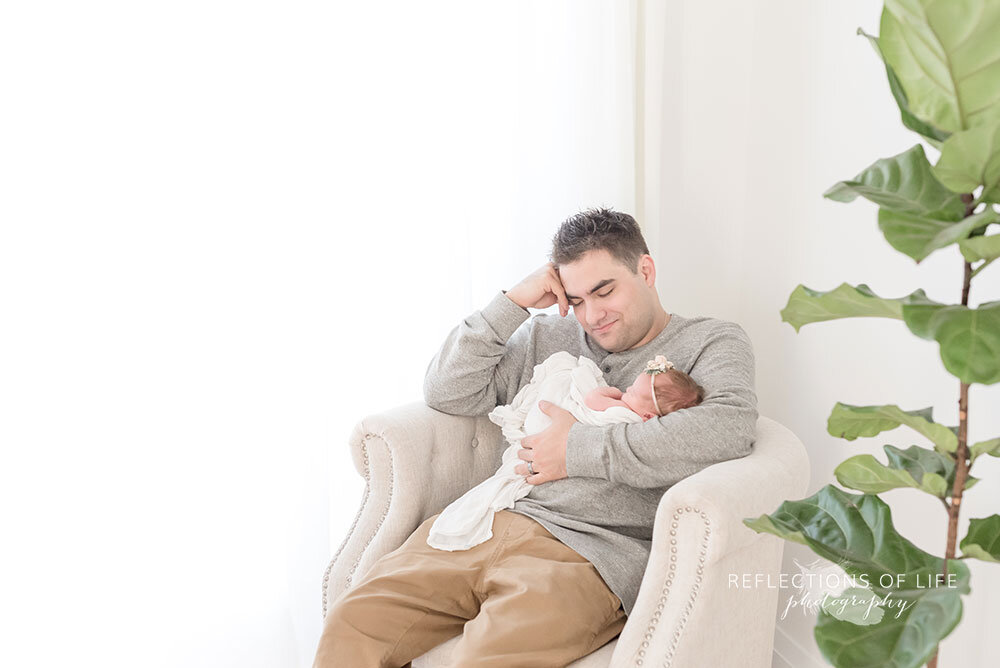 Daddy falling asleep with newborn baby girl in his arms during family photoshoot in Grimsby photo studio