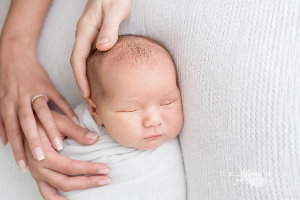 Newborn baby boy with parents hands on his head Niagara photo studio