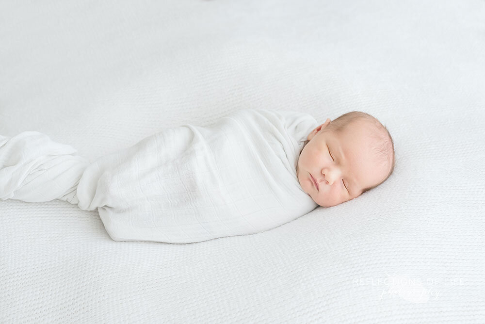 Newborn baby boy swaddled in little unicorn white swaddle blanket in Niagara Region Photo Studio
