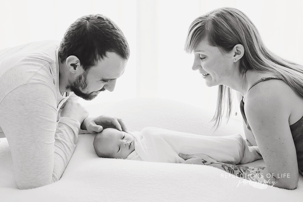 Parents-leaning-over-newborn-baby-swaddled-Niagara-newborn-photography-southern-Ontario