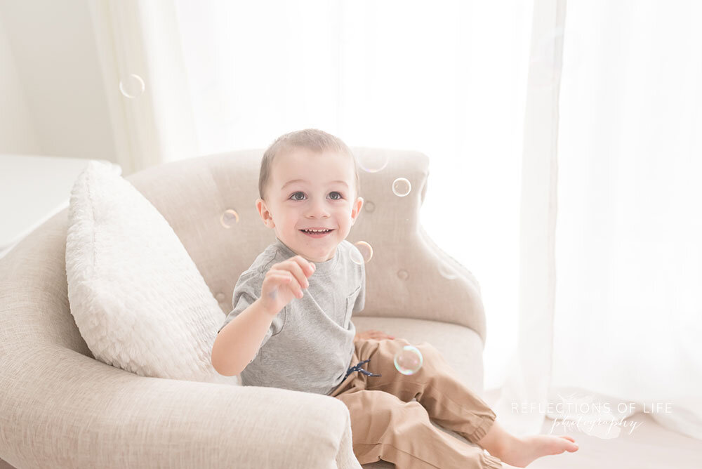 Little-boy-sitting-on-tufted-chair-surrounded-by-bubbles