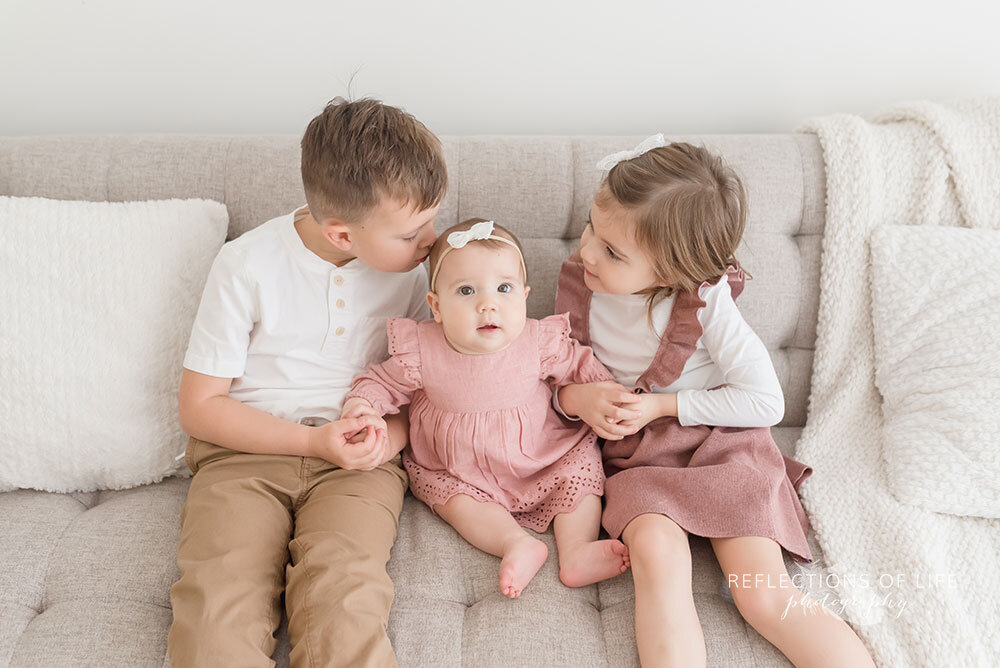 Siblings Sit on a Couch with New Baby Sister