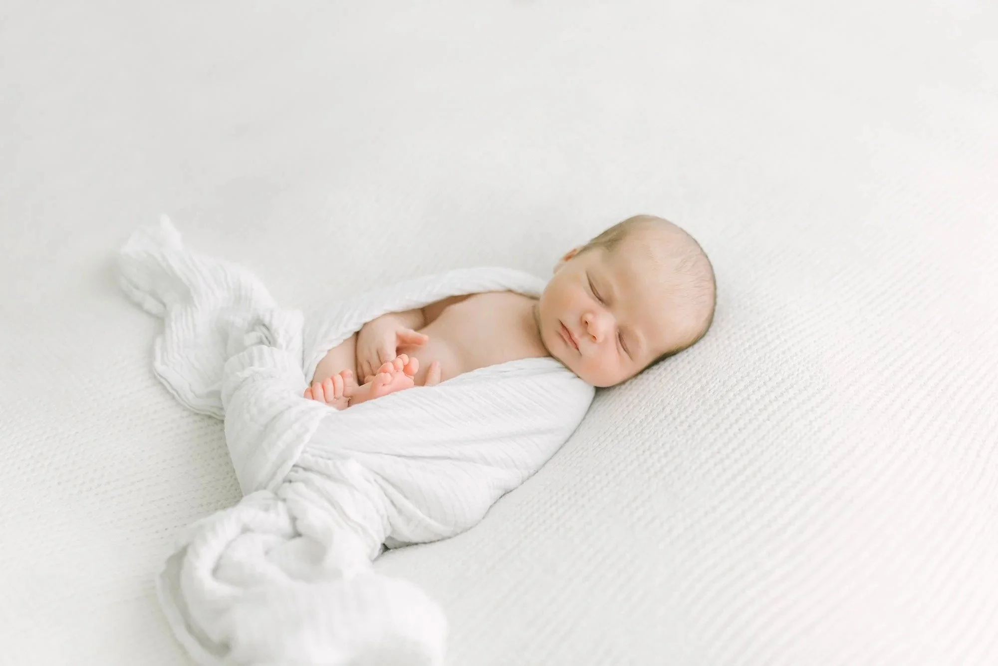 Sleeping baby wrapped in white captured by Hamilton Newborn Photographer at studio by Reflections