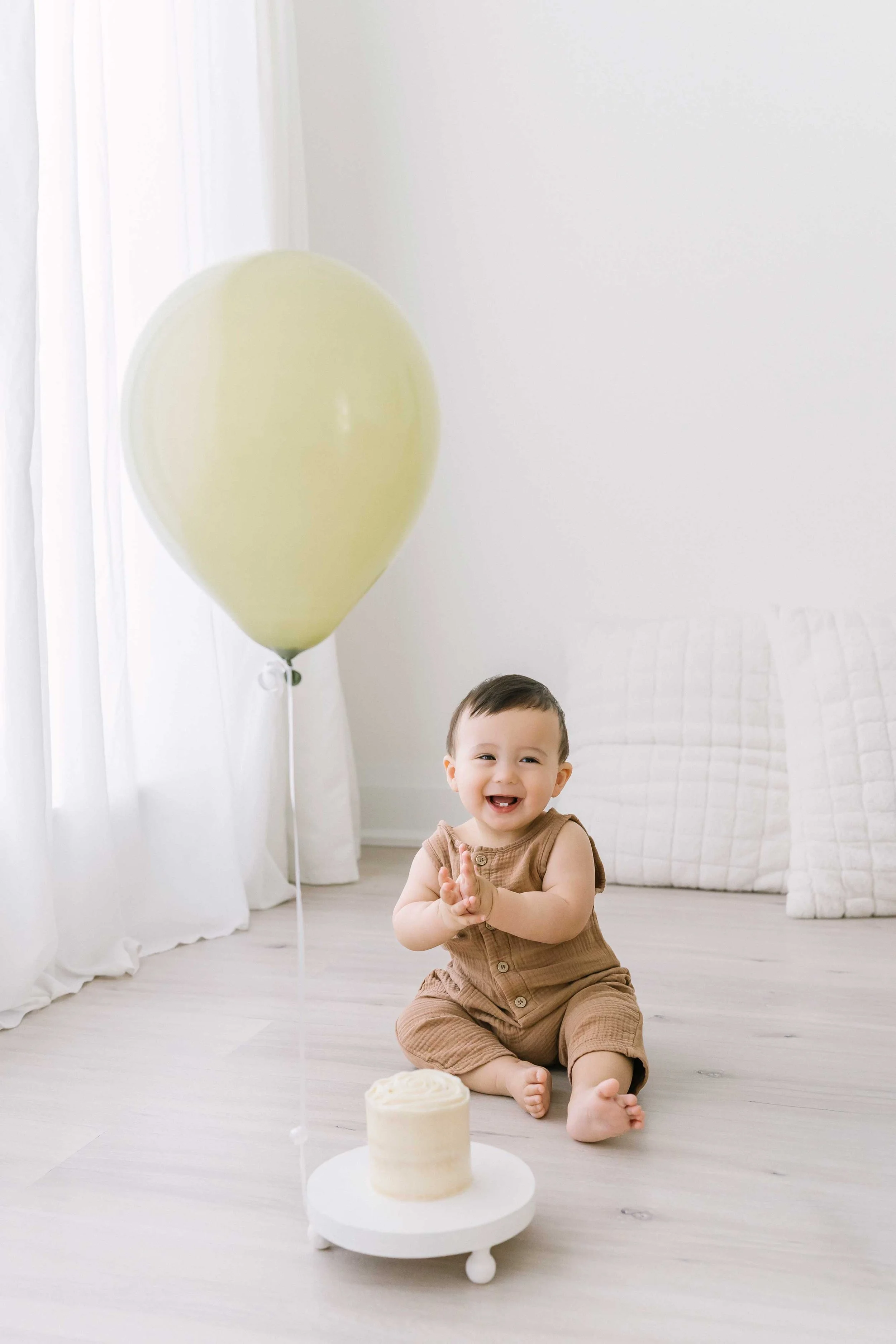 Adorable cake smash photography session featuring a curious one-year-old baby boy tasting birthday cake frosting for the first time.