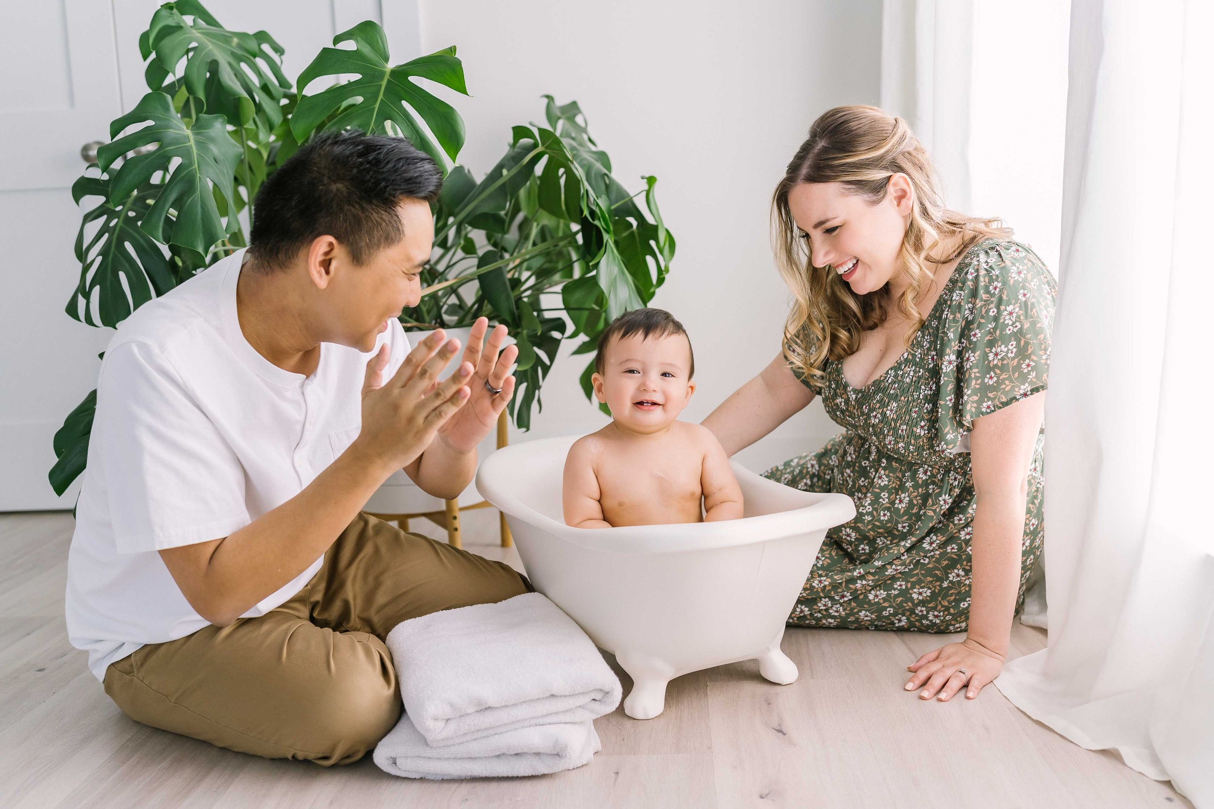 Bubble bath photography session featuring a smiling one-year-old baby boy splashing in warm water after his cake smash celebration.
