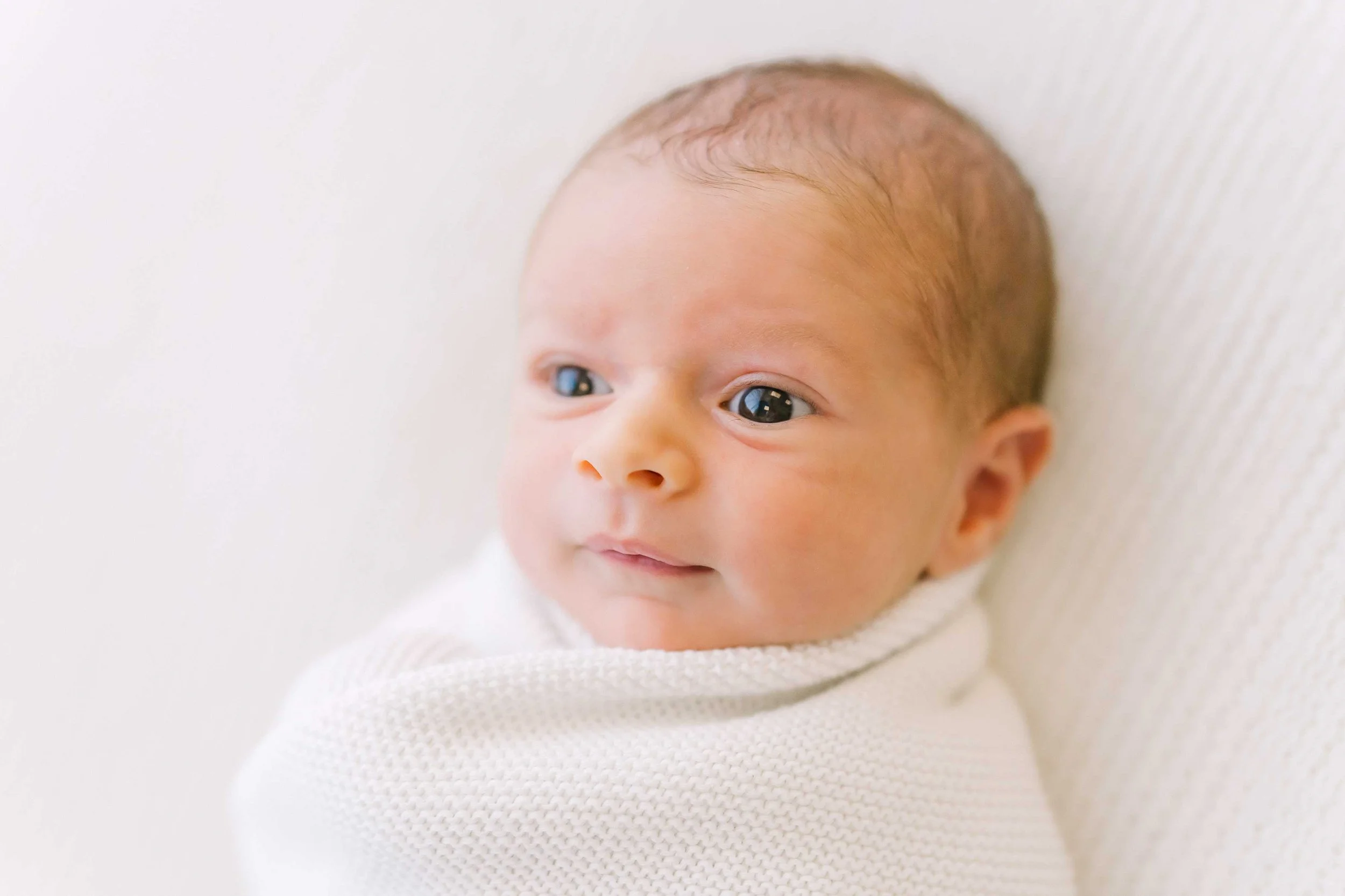 Wide awake newborn baby wrapped in cream blanket during newborn photography session in Grimsby