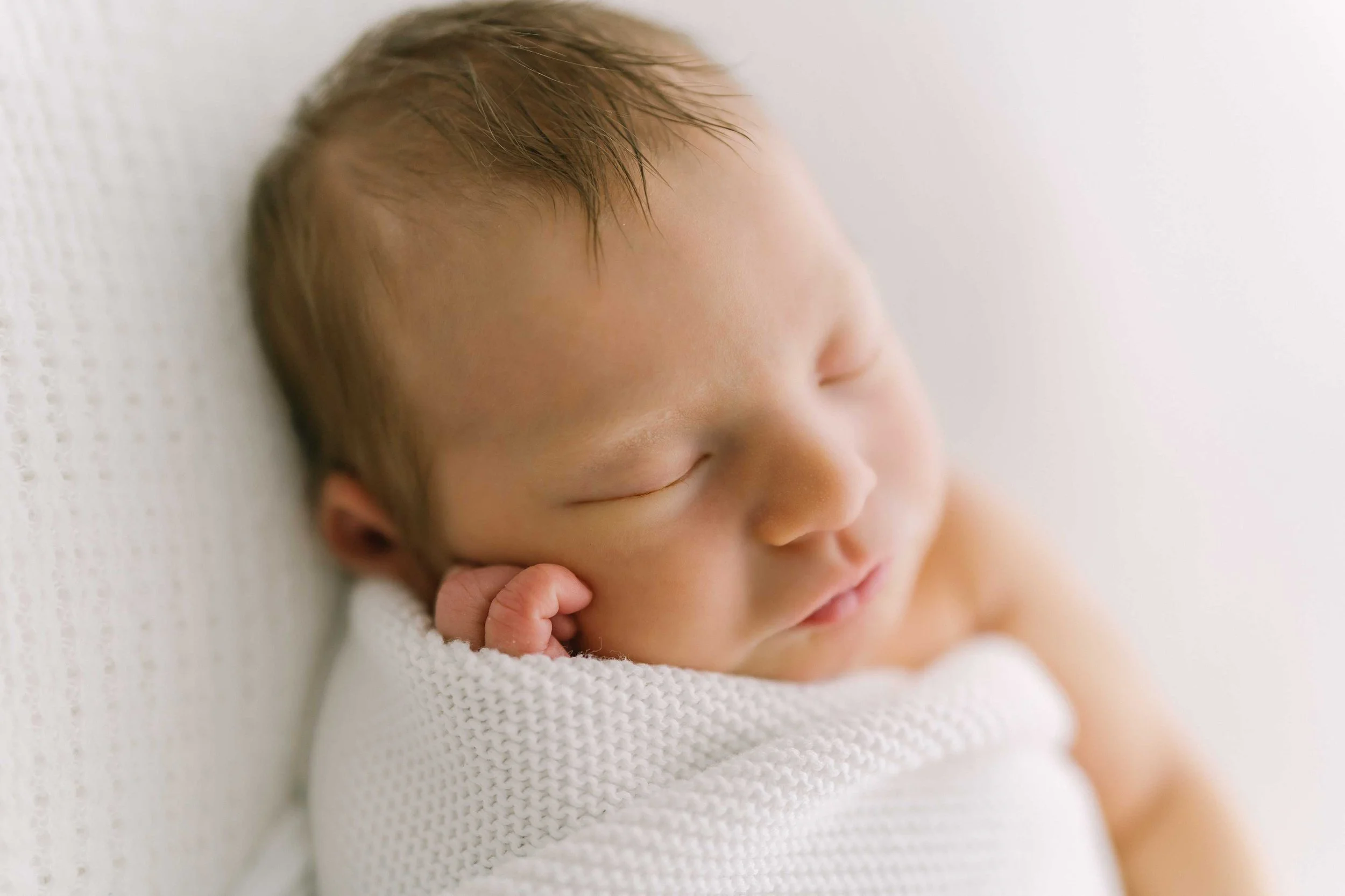 Peacefully sleeping newborn wrapped in white blanket during newborn photography session in Grimsby studio