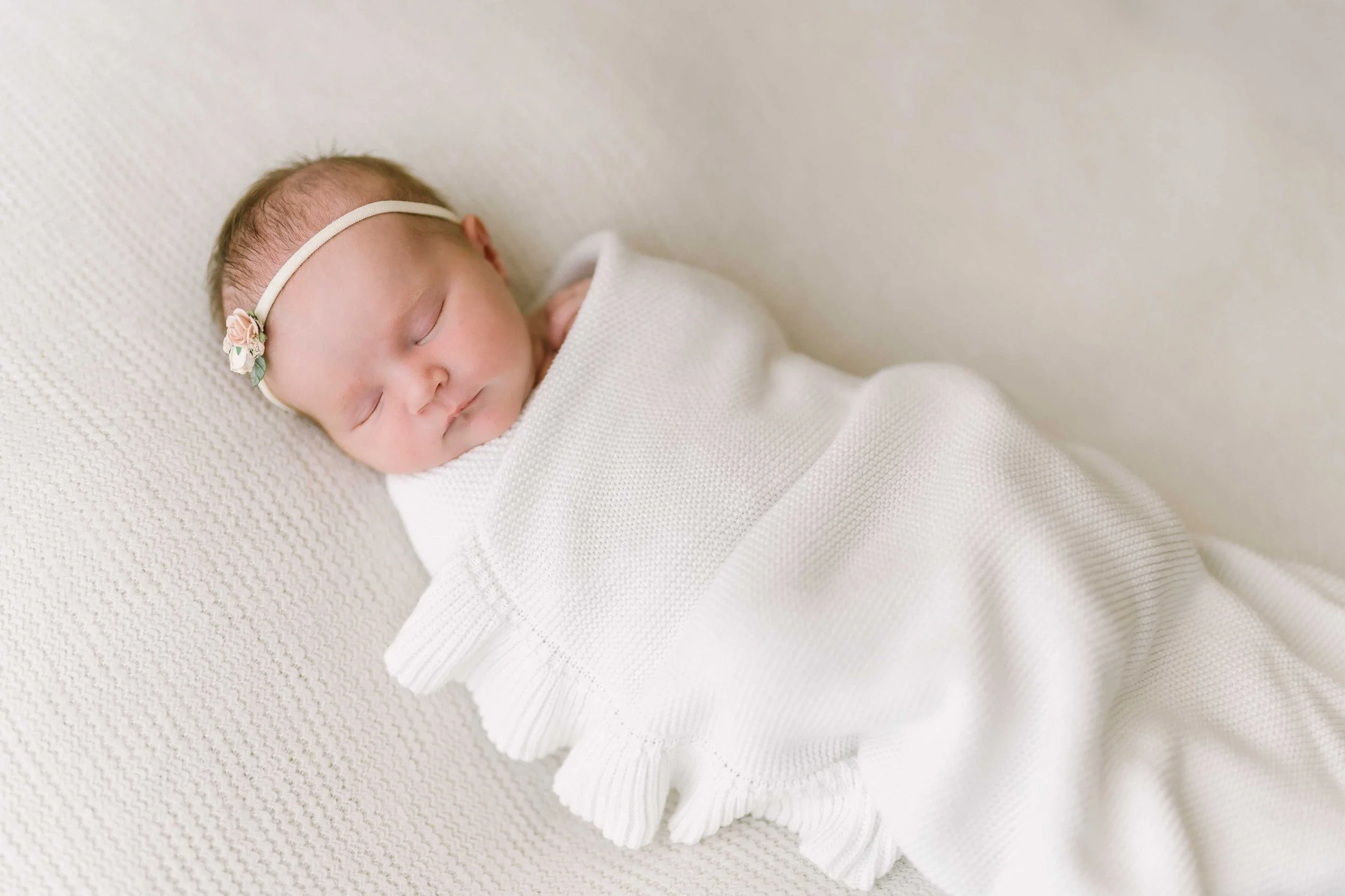 Sleeping newborn baby girl wrapped in white during newborn photography session in Grimsby