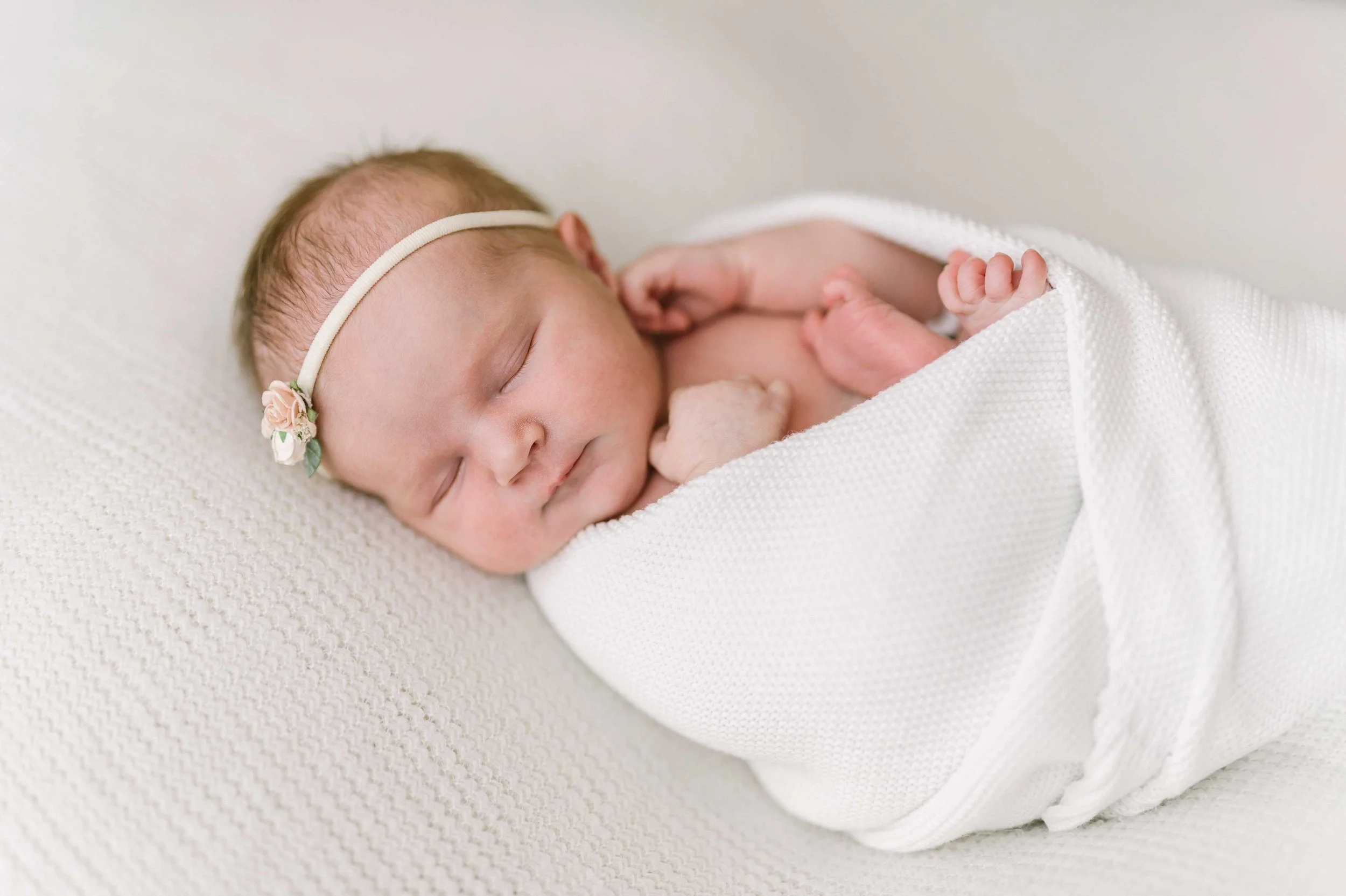 Peacefully sleeping newborn with cream wrap and soft neutral blanket at Reflections studio