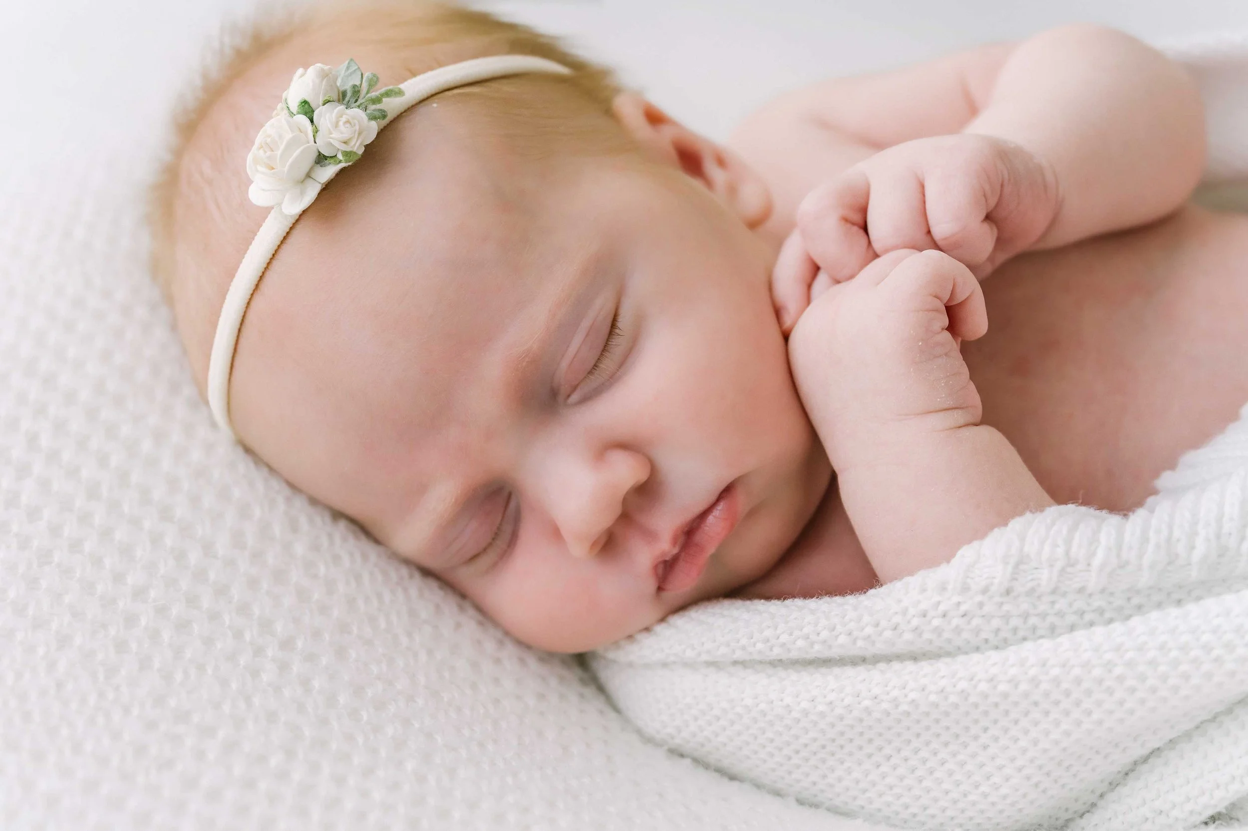 Close-up of newborn baby girl’s tiny hand resting against her cheek