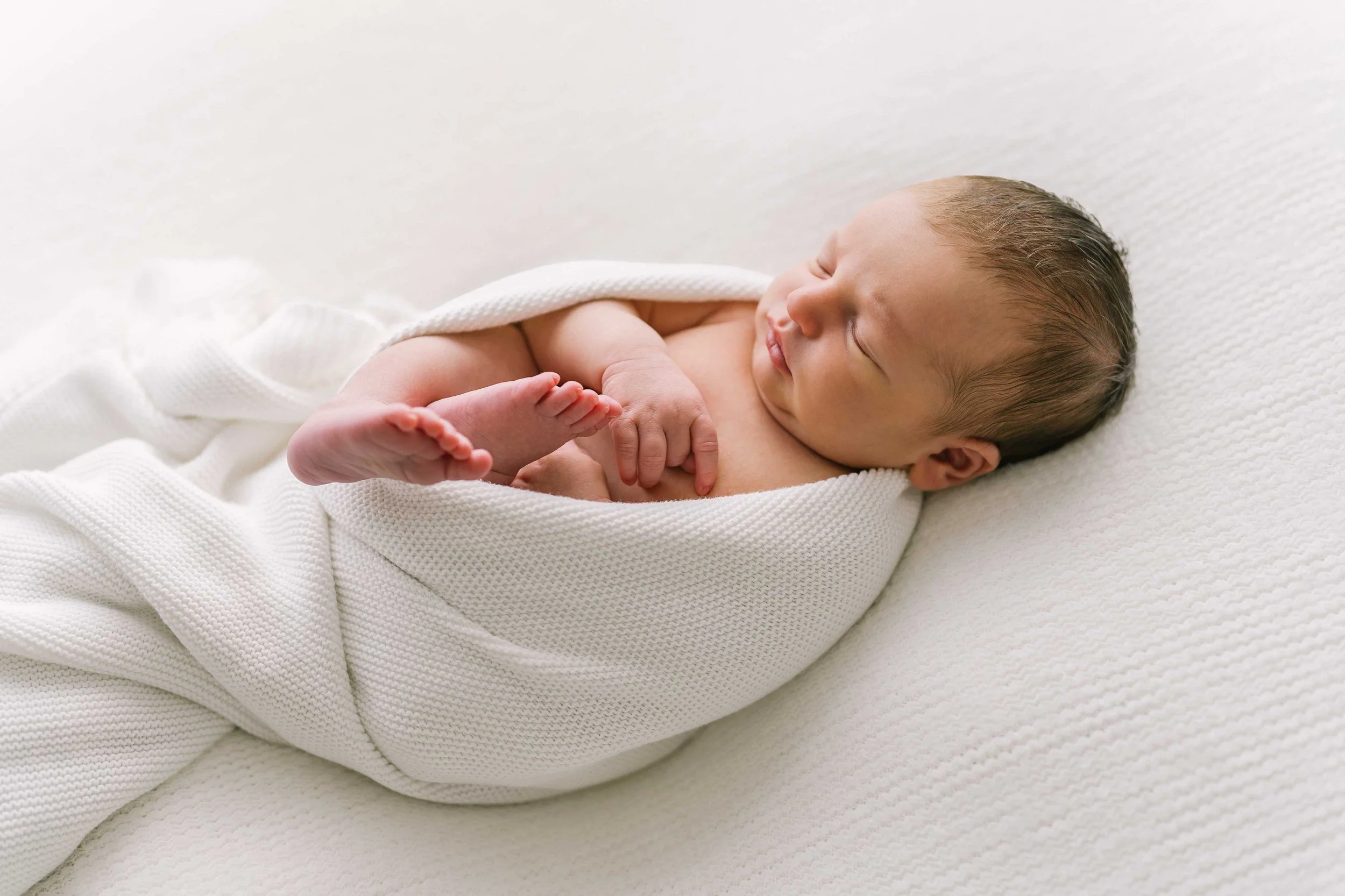 Full-body photo of newborn baby boy peacefully wrapped in a neutral blanket