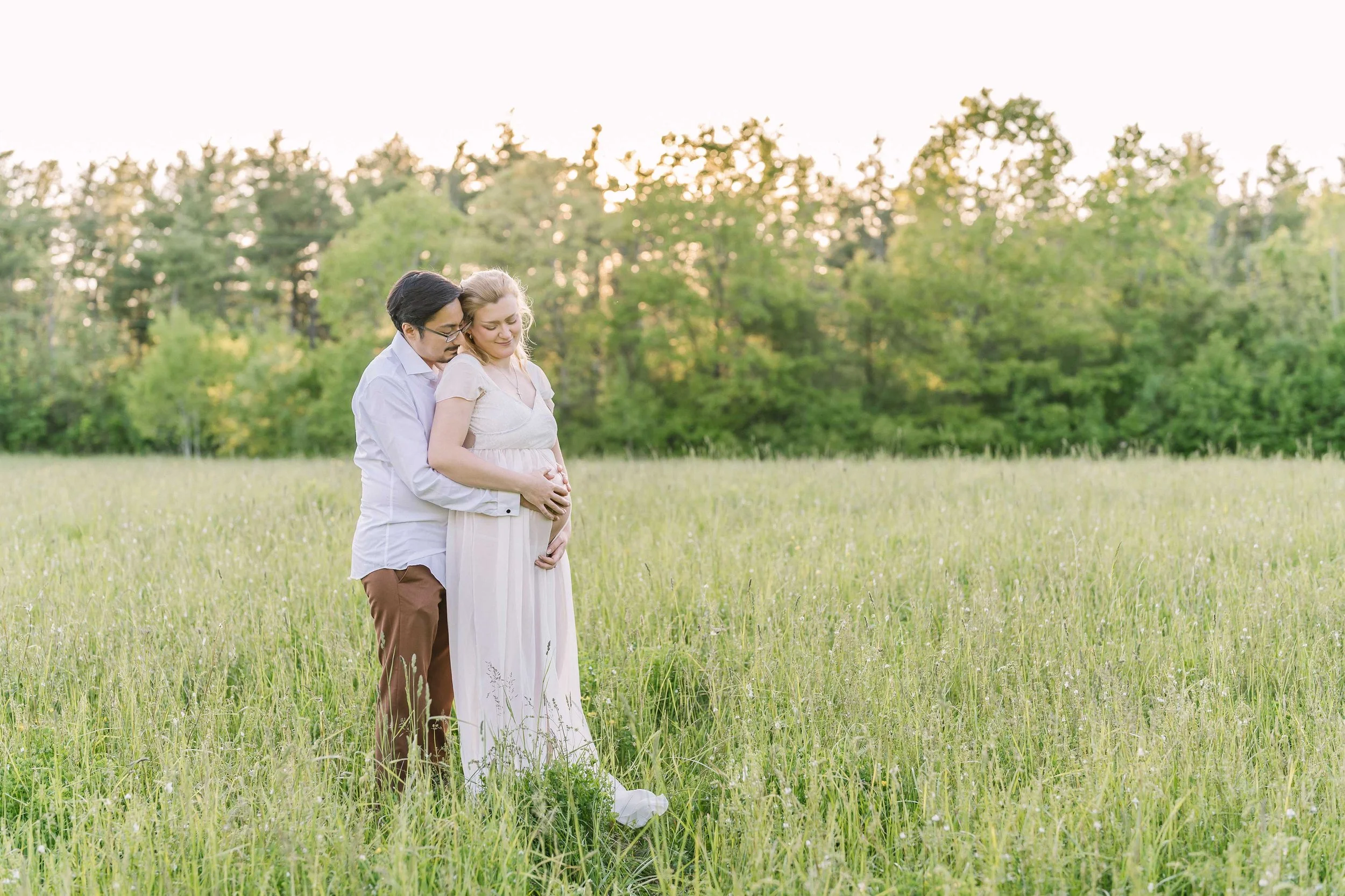 Maternity couple standing in a Grimsby field during golden hour