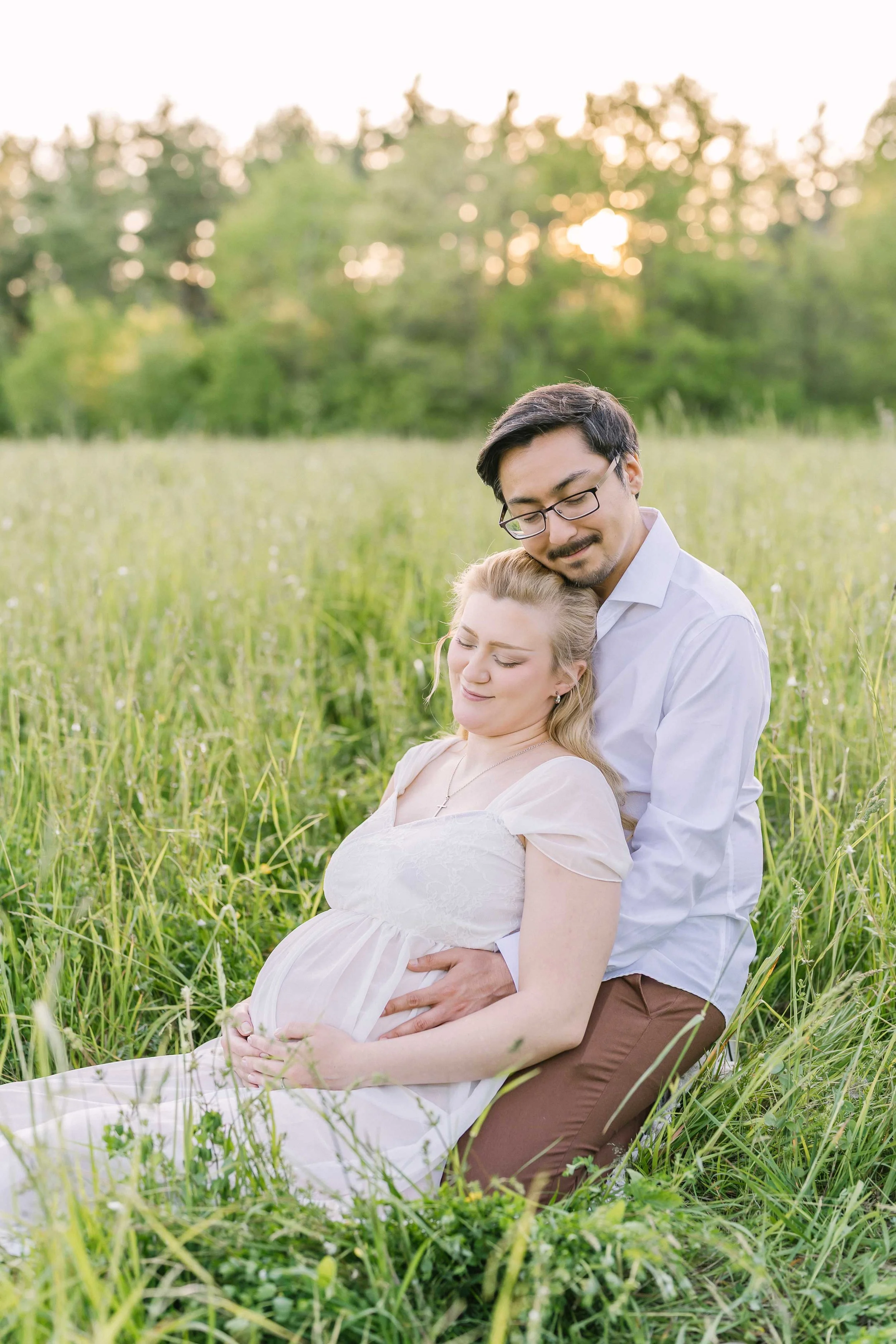 Pregnant couple sitting together in a field during outdoor maternity photography