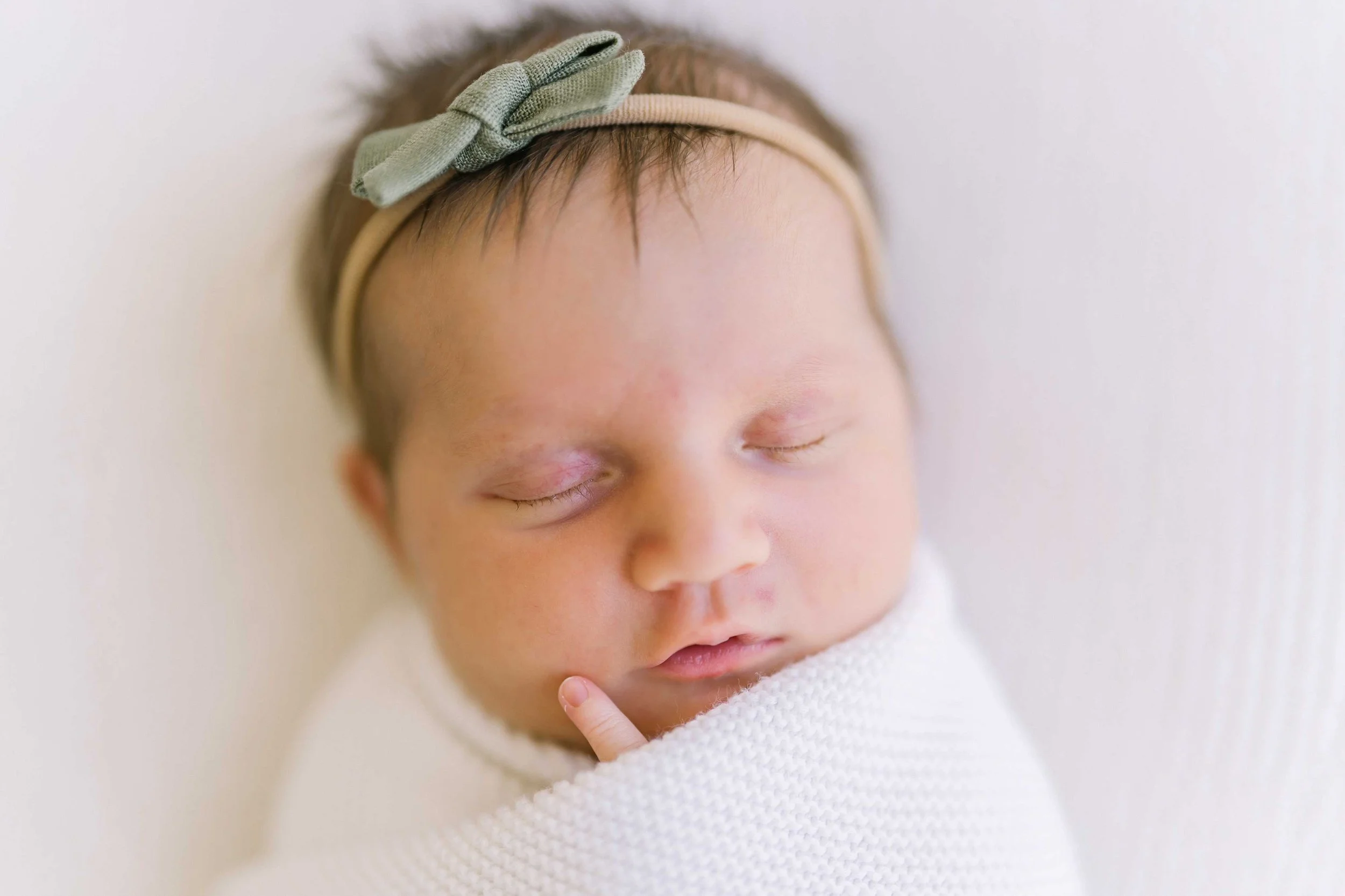 Sleeping newborn baby girl in a green bow headband, wrapped in white in our Grimsby studio