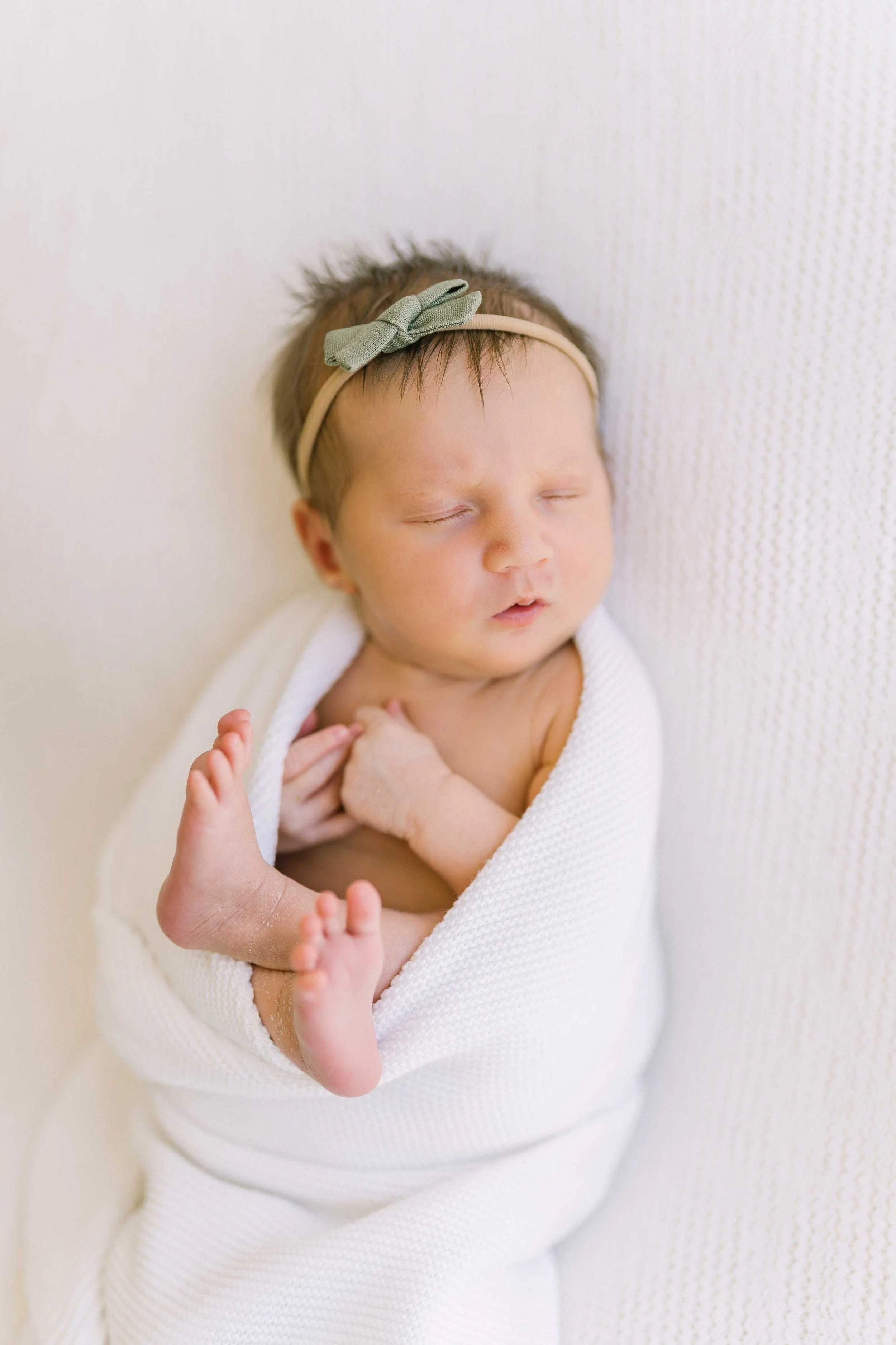 Sleeping newborn baby girl wrapped in white with her tiny toes peeking out, photographed from above in Grimsby