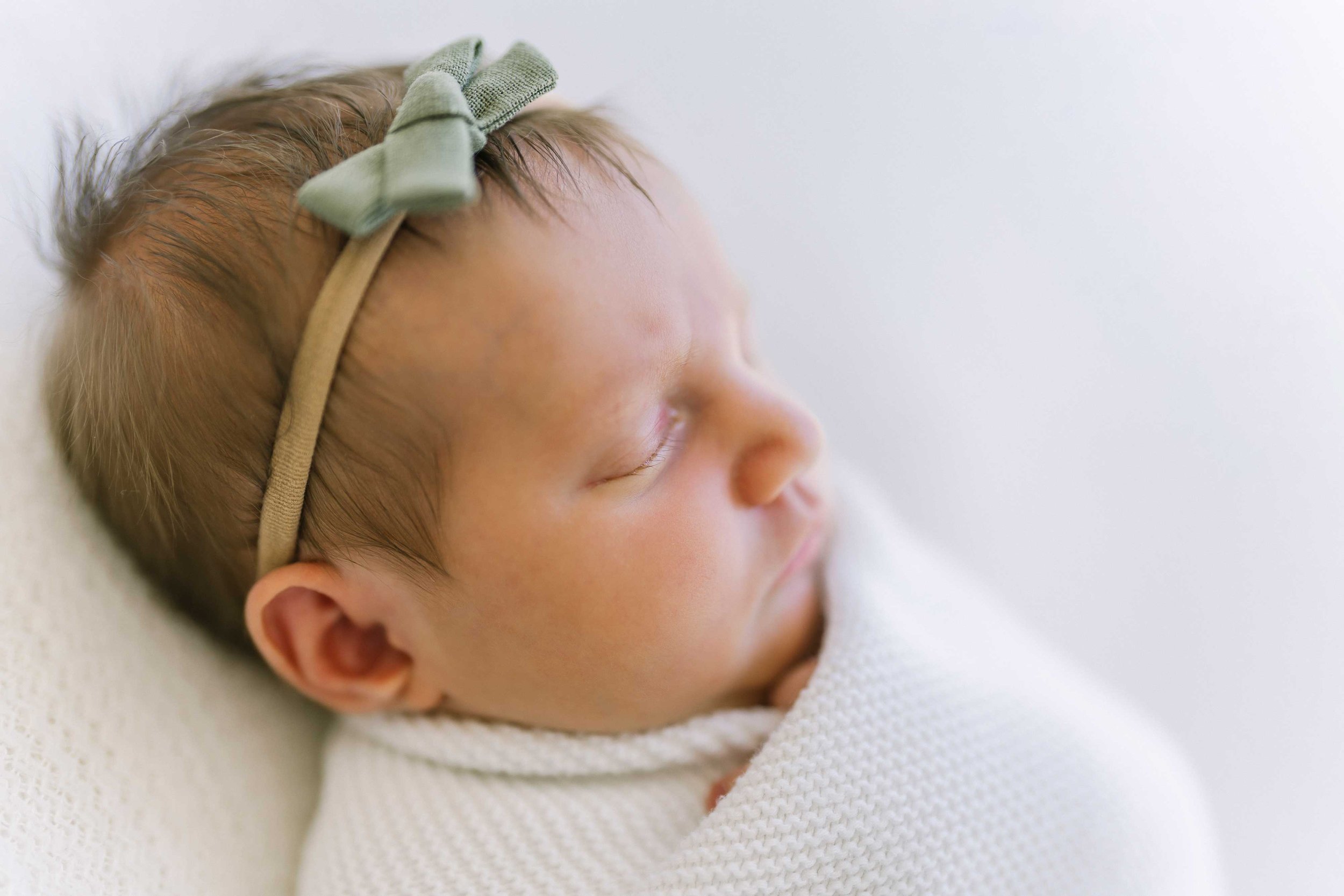 Newborn baby girl asleep with a soft green bow during a Grimsby newborn photography session