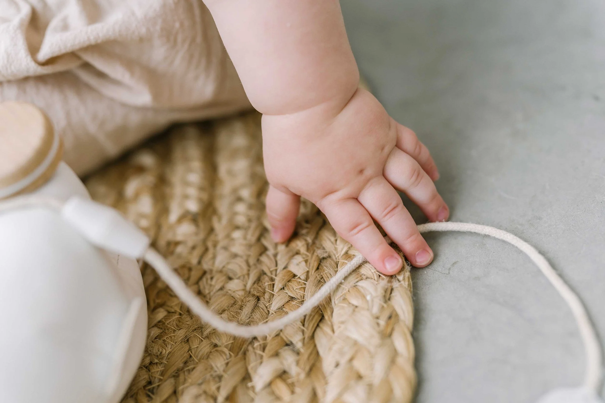 Close-up of a baby's chubby hand reaching across a woven rug during her baby milestone photos