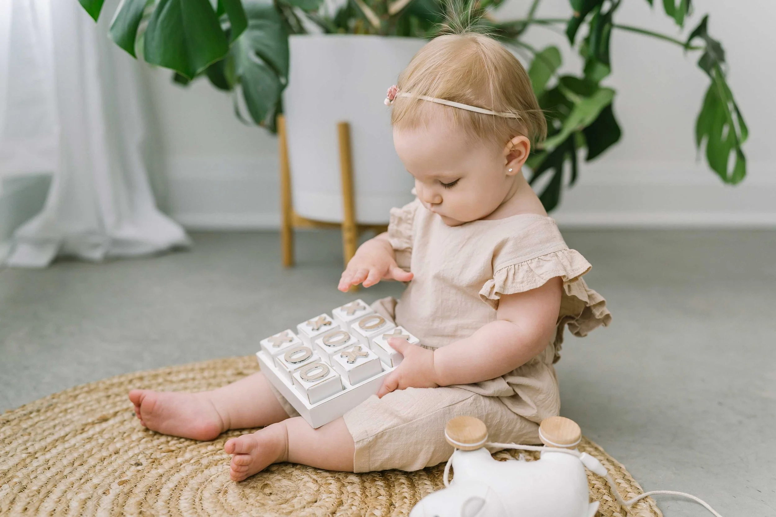 Baby girl sitting on a woven rug playing with a wooden toy during her first year photos in Grimsby