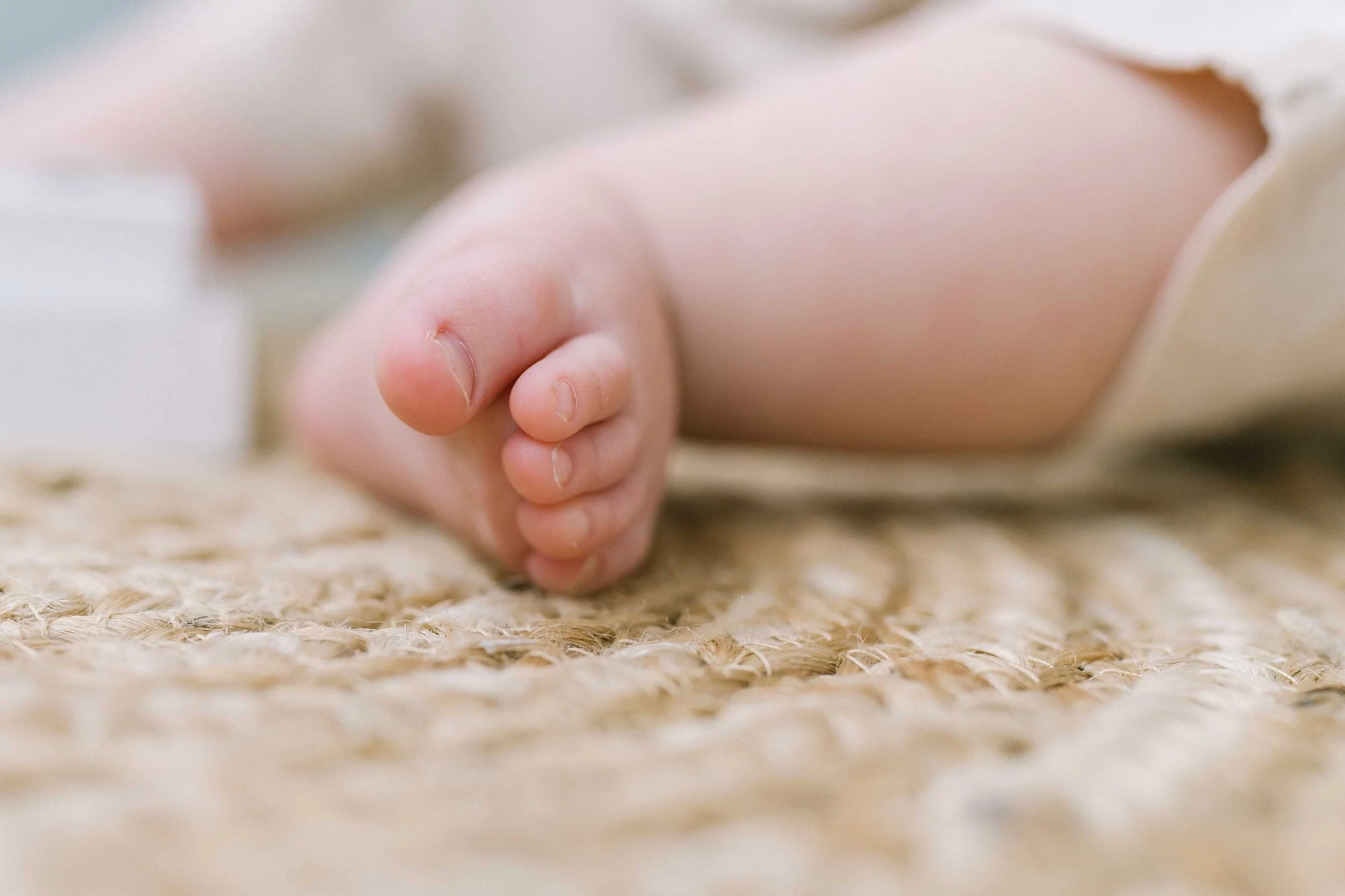 Close-up of a baby girl's tiny toes on a woven rug during her baby milestone photos