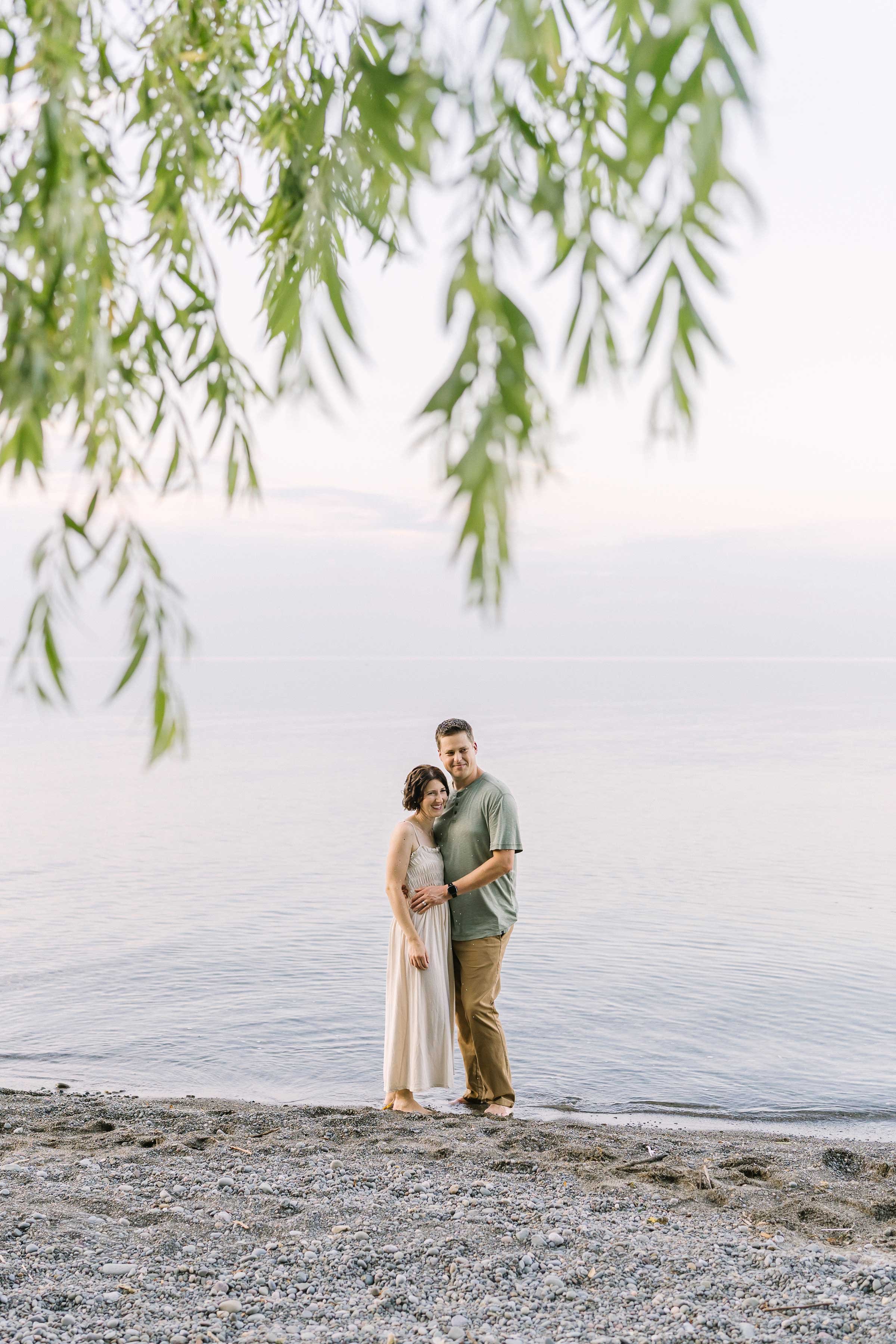 Mom and dad hugging at the edge of Lake Ontario under a willow tree in Niagara