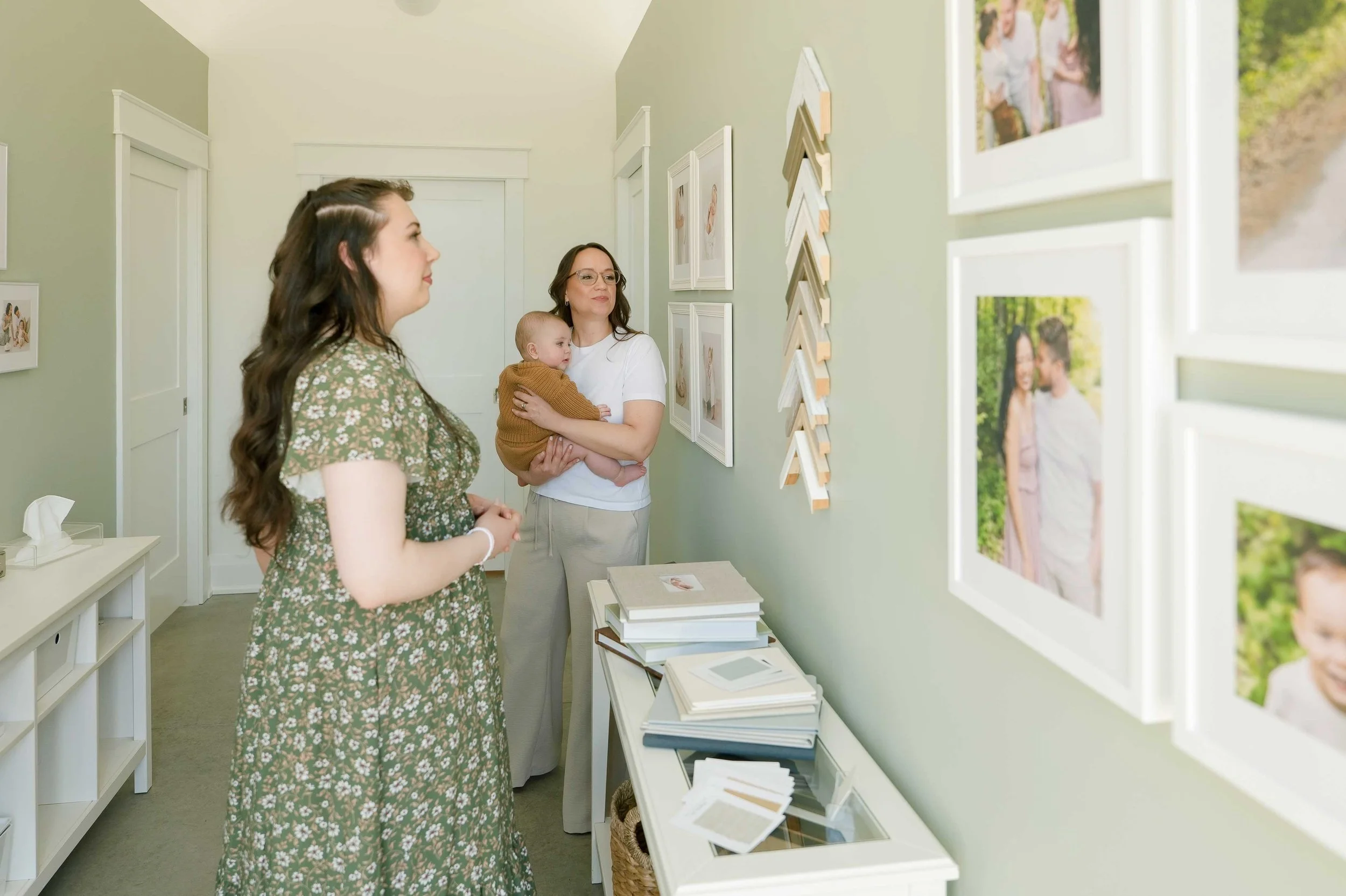 Mom holding baby viewing framed family portrait gallery wall in Grimsby home
