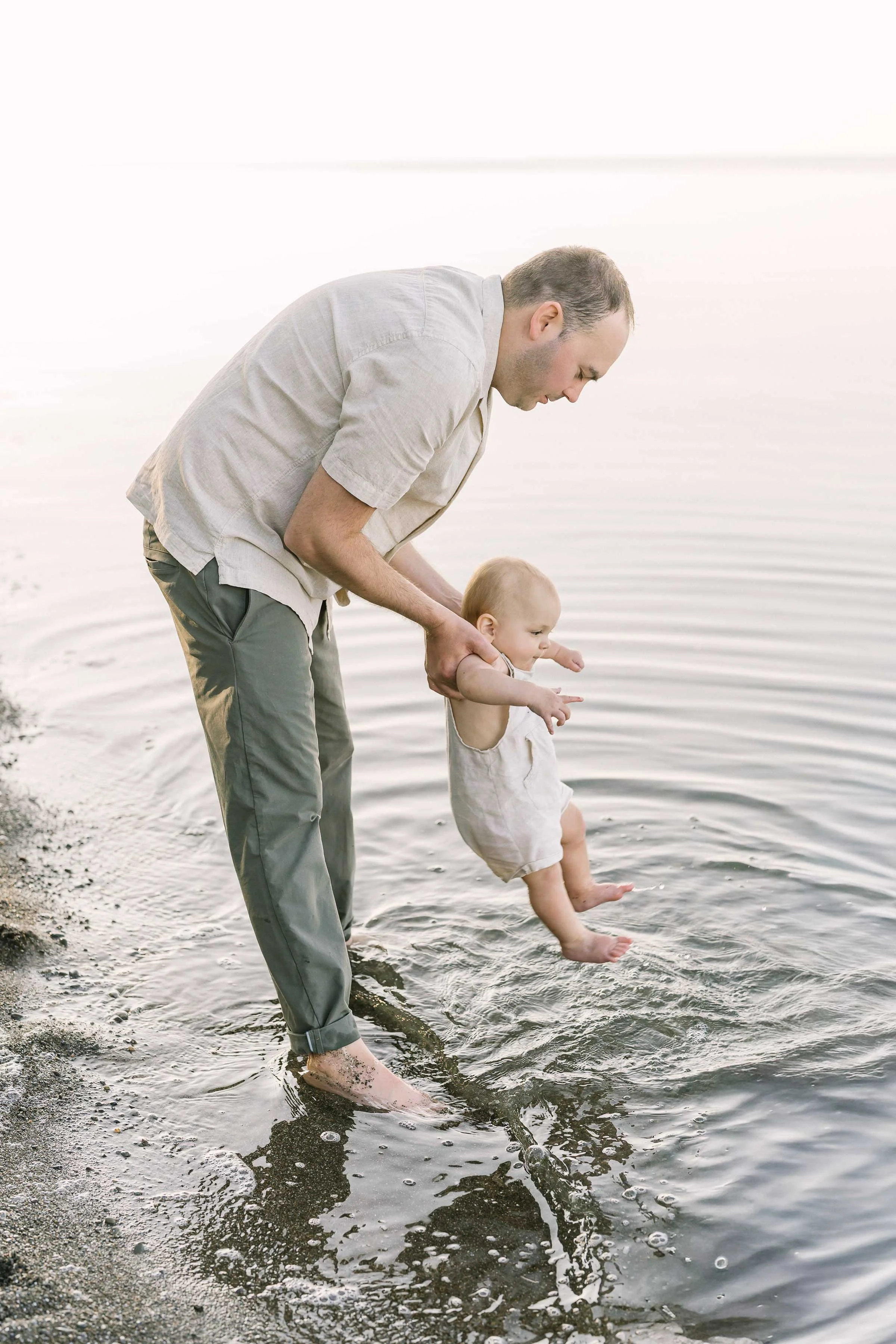 Dad dipping his baby's toes in Lake Ontario during a family session in Niagara
