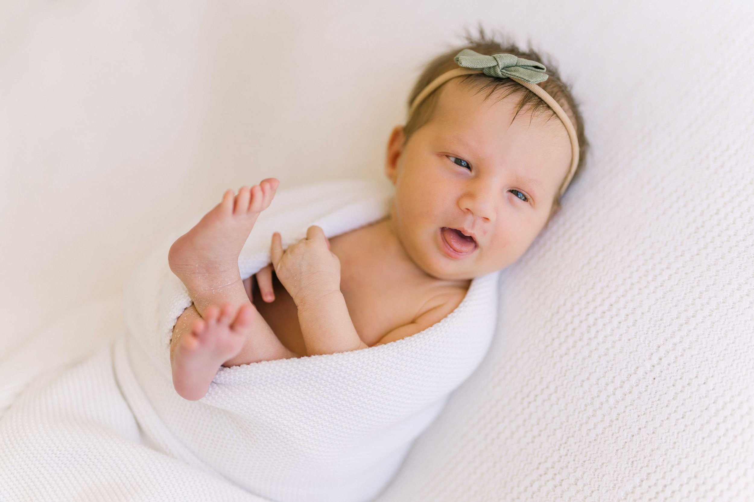 Wide-awake newborn baby girl with her mouth open and one foot kicked up during a Niagara newborn session
