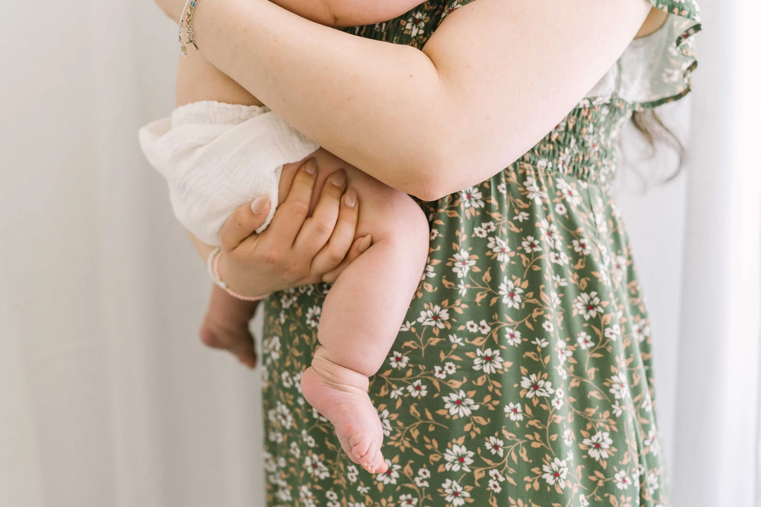 Mom holding baby's foot in floral dress during newborn photography Grimsby session