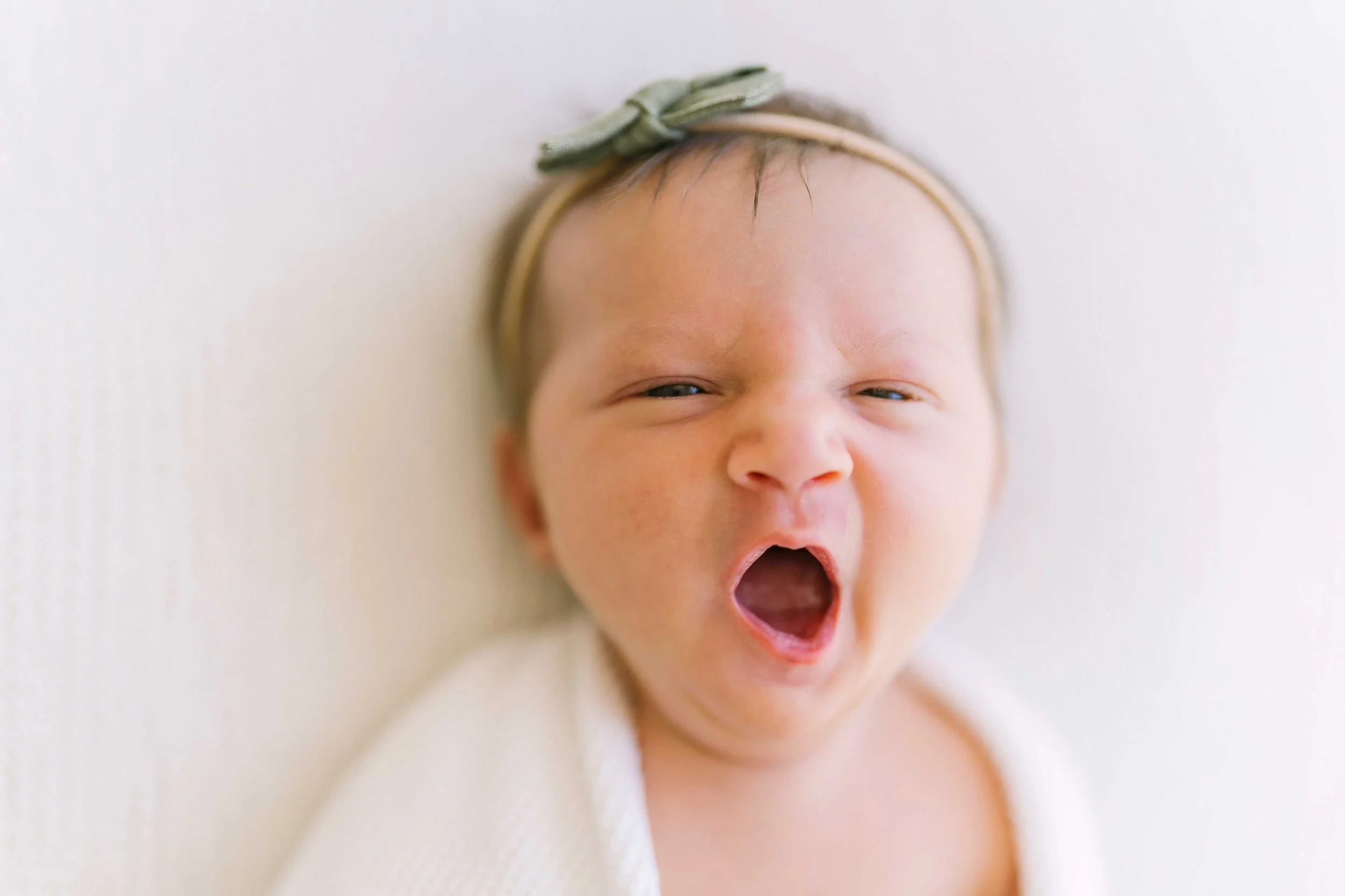 Newborn baby girl in a green bow headband mid-yawn during her Grimsby newborn photos