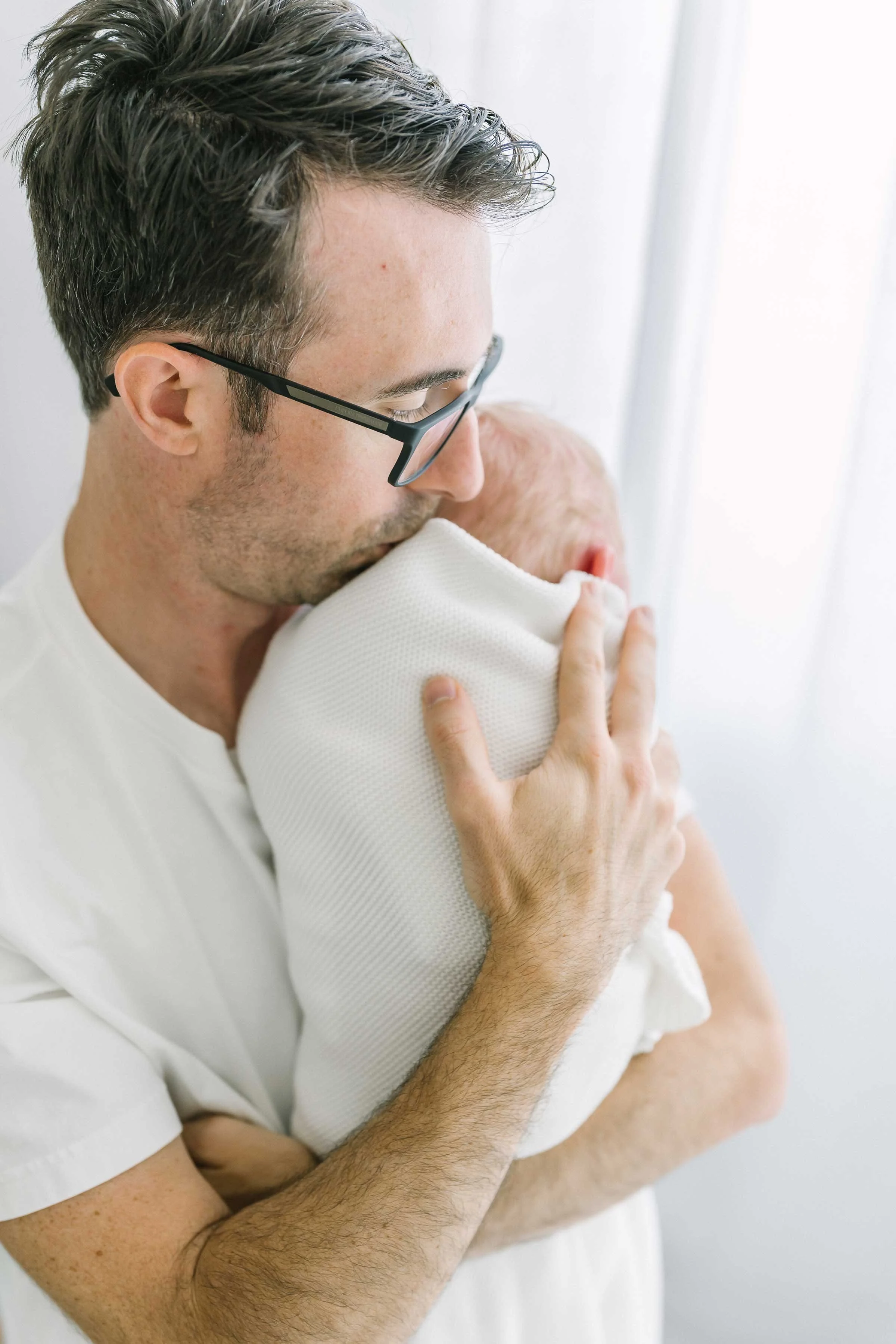 New dad kissing his swaddled newborn baby during a newborn session in Niagara