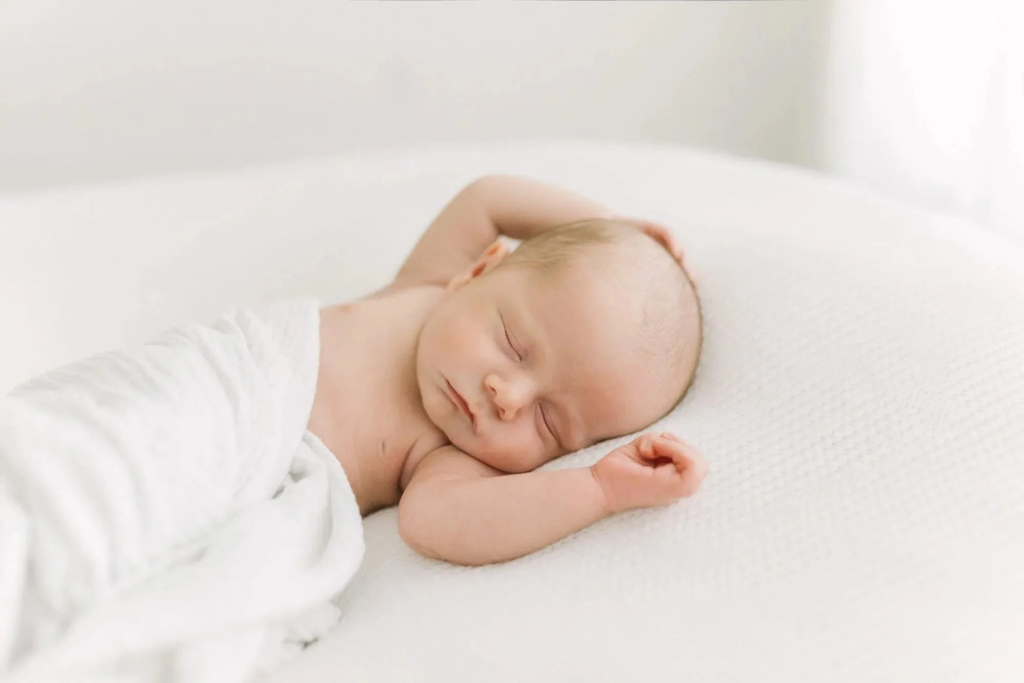 A close-up photo of a sleeping newborn baby wrapped in a soft blanket, peacefully nestled in a cozy basket, capturing the innocence and tenderness of early life at a full-service newborn photography studio in Niagara.
